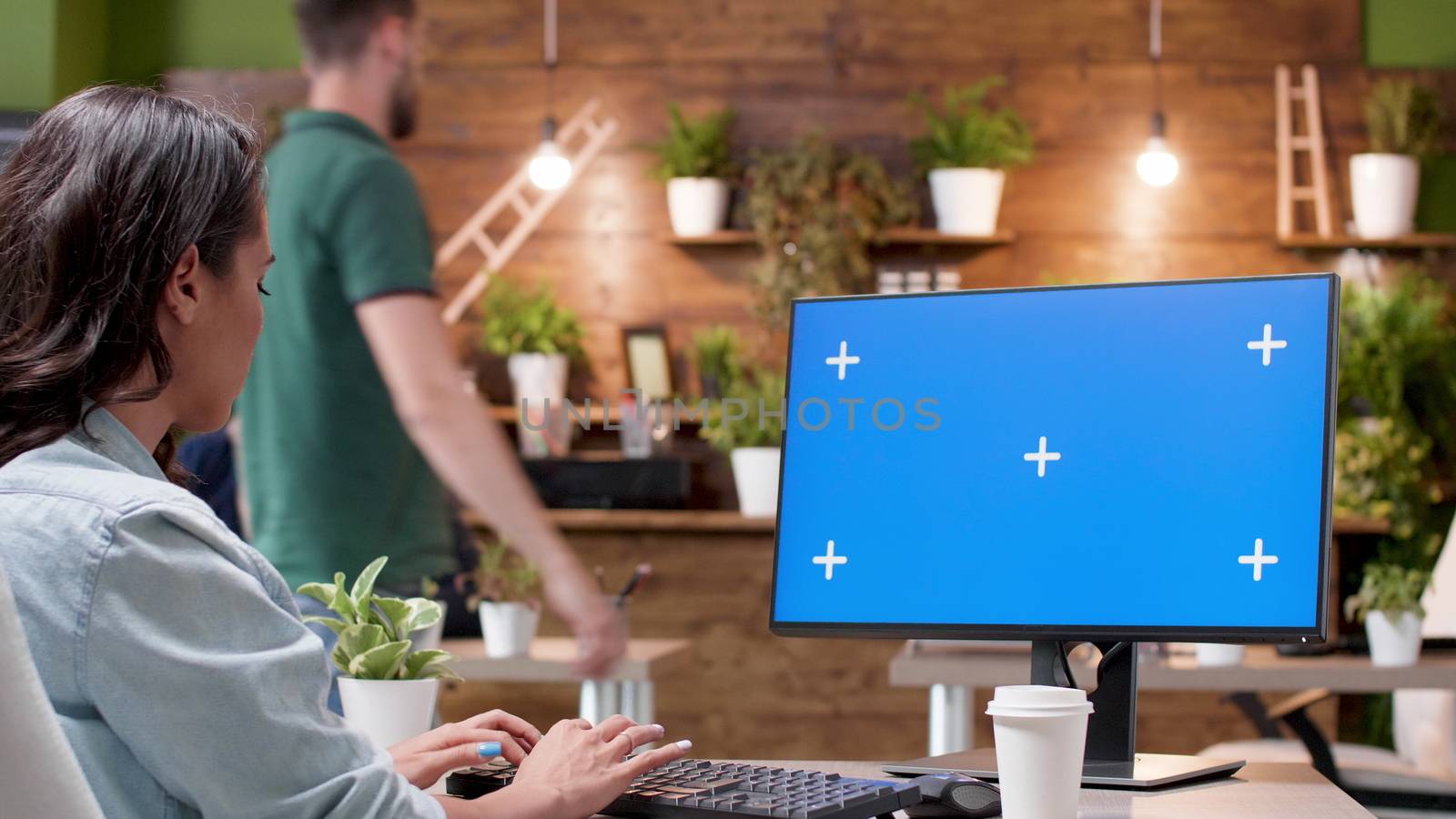 Woman typing on computer and sips coffee in front of a screen mock-up in a cozy and modern office environment