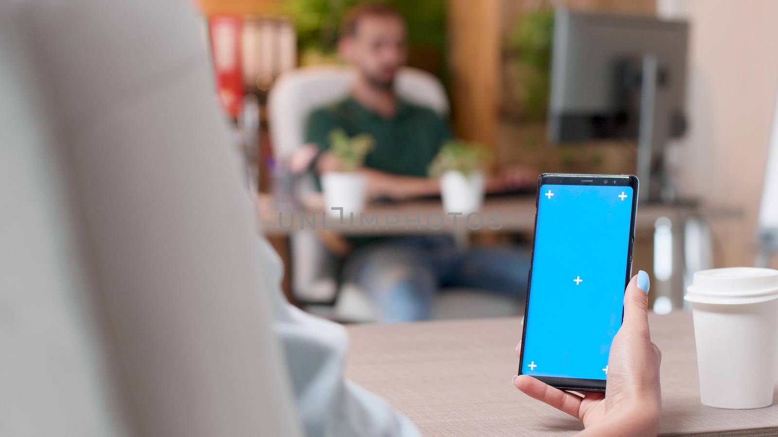 Woman holds a phone with an isolated blue screen mock-up in busy office environment