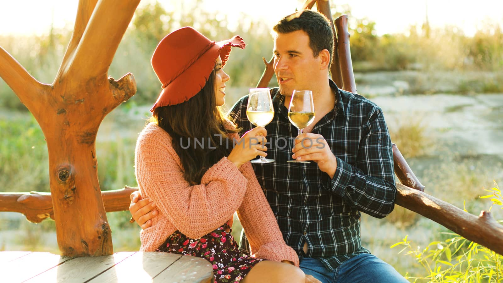 Beautiful caucasian couple in sun flares clinking glasses with white wine.
