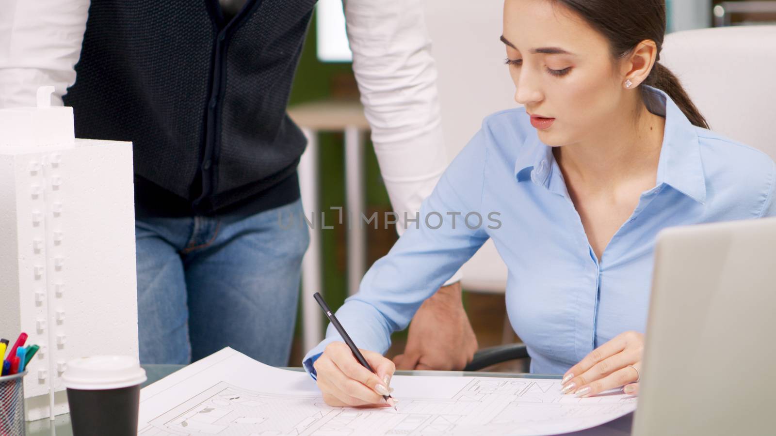Construction engineer talking with female architect and drawing on blue print. Building model.
