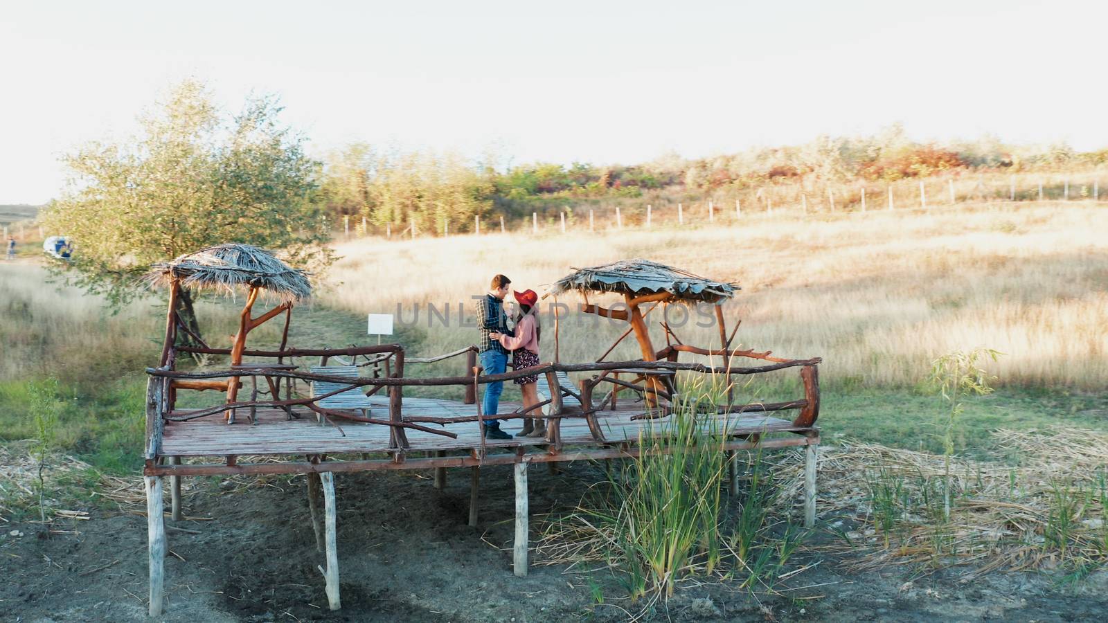 Beautiful couple clinking glasses with wine on a pontoon in a rural area, aerial drone shot
