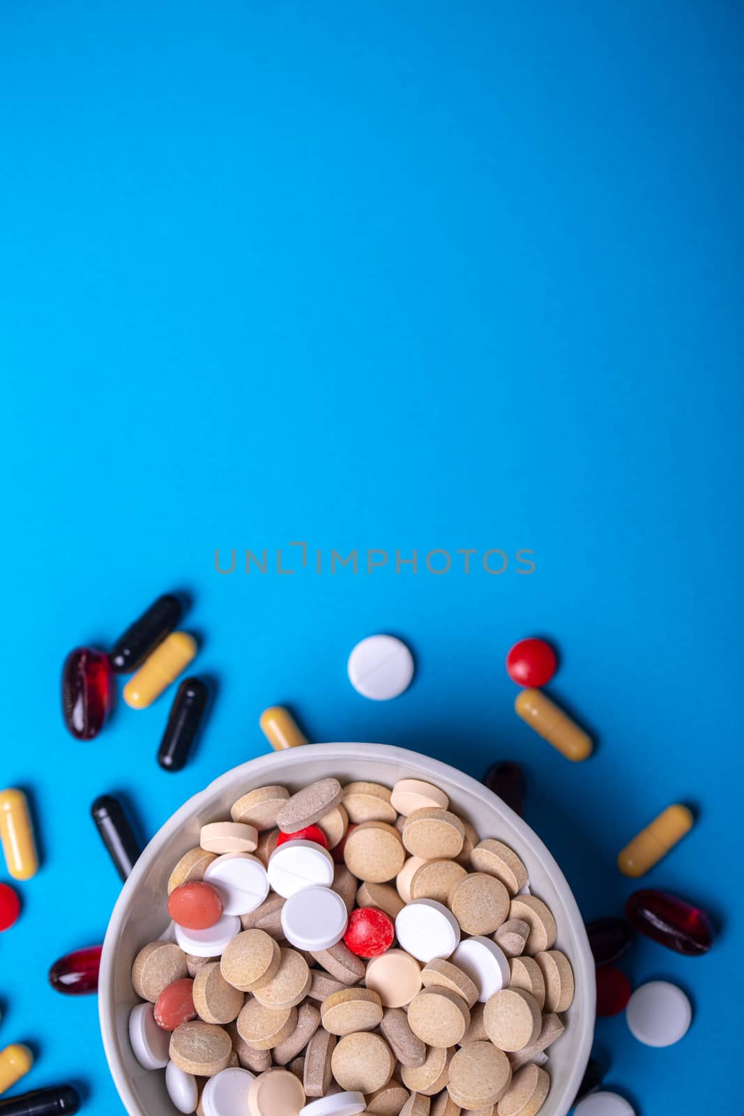 Top view with a bowl with pills of different colors and a place for copy space. Macro and blue background