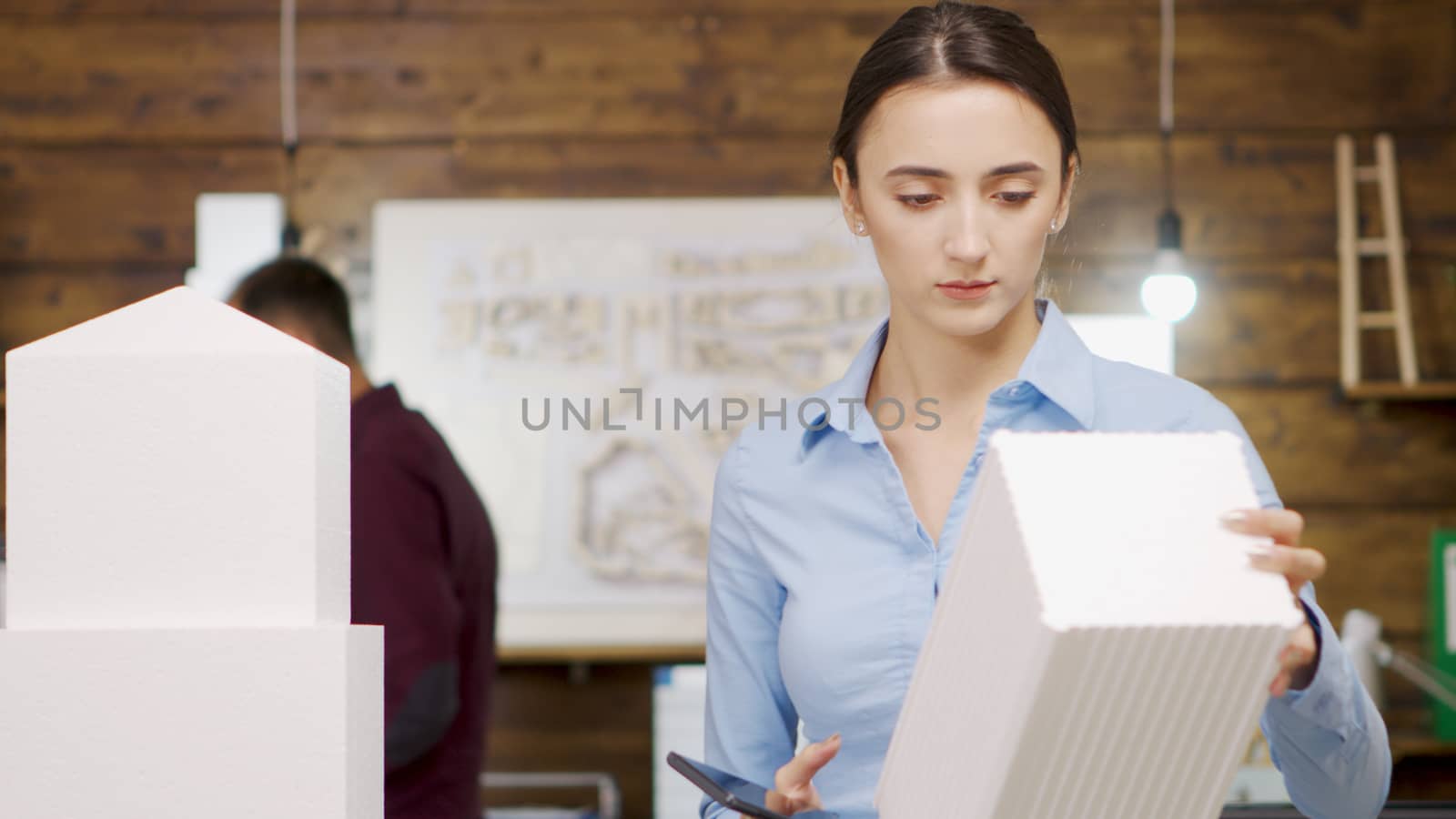 Close up of female architect taking photos of building model of sky scraper. Female architect using smartphone.