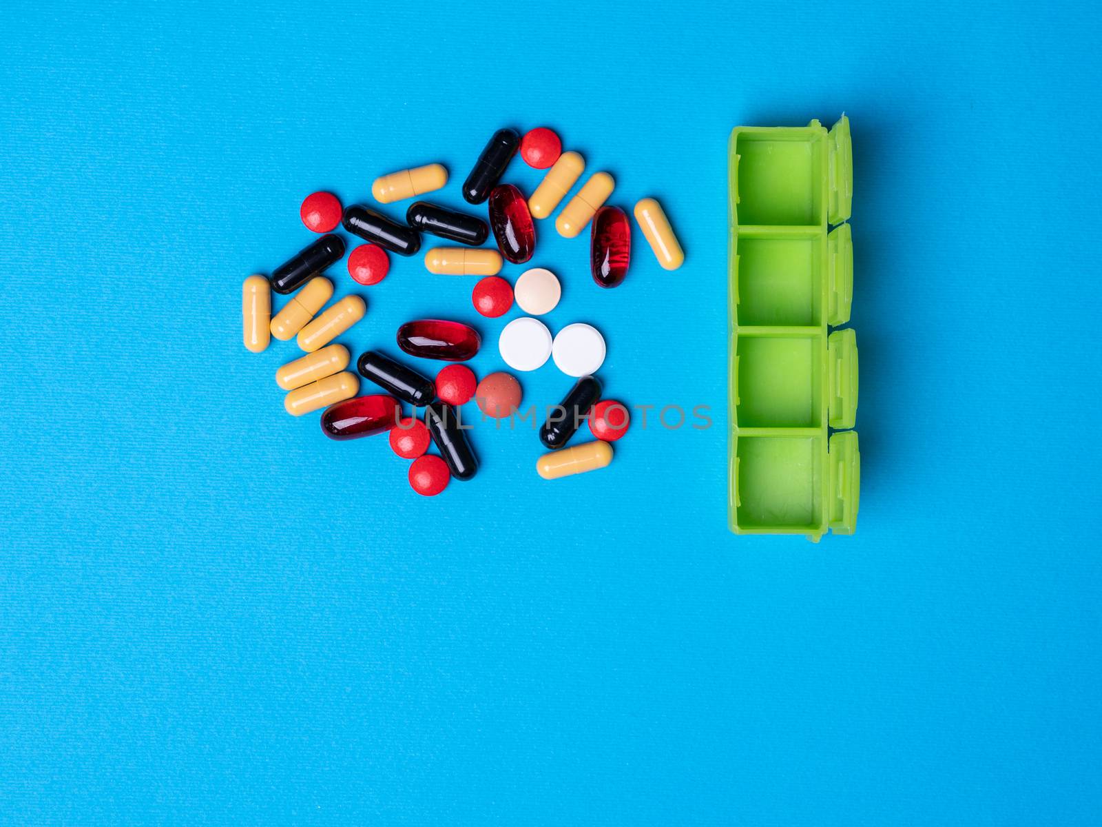 Top view with a green organizer and next to multicolored pills and capsules. Blue background and copy space