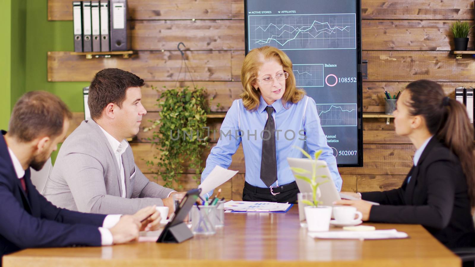 Caucasian executive female giving her young team new charts to study. Important business meeting.