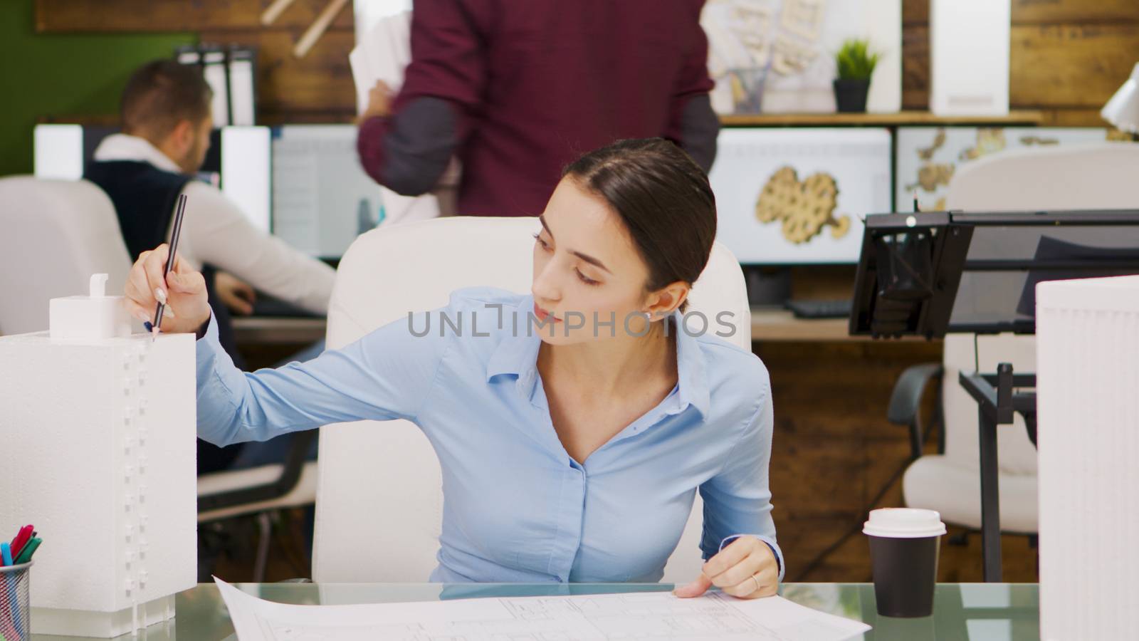Young female architect working on a building project and taking a sip of coffee. Building model.