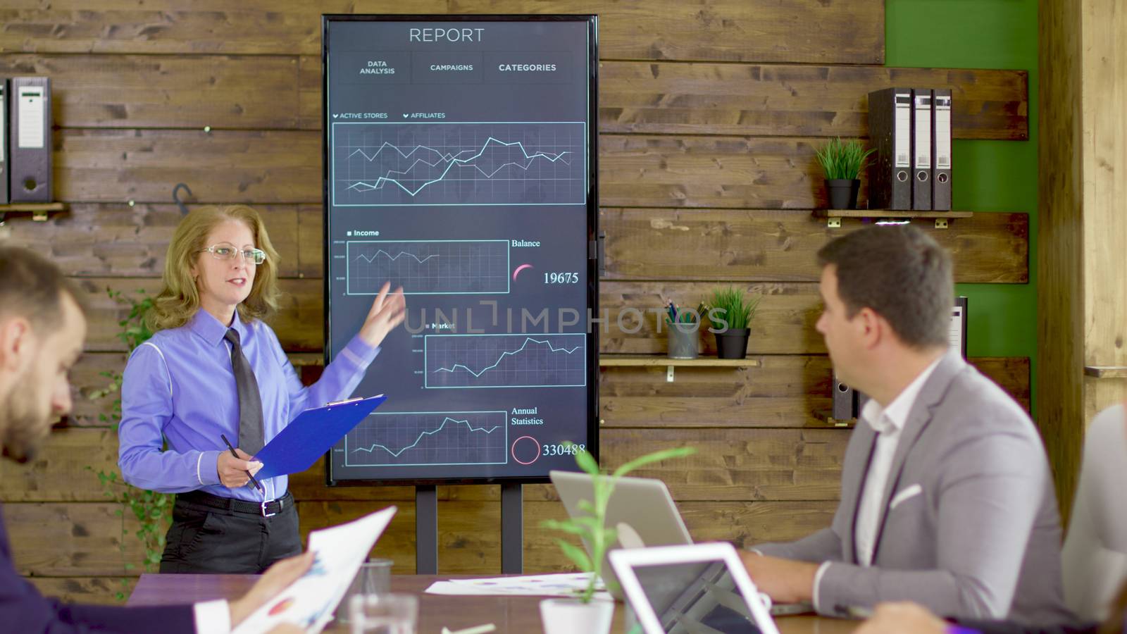 Female in a conference room pointing at statistics on tv screen. Team breefing.