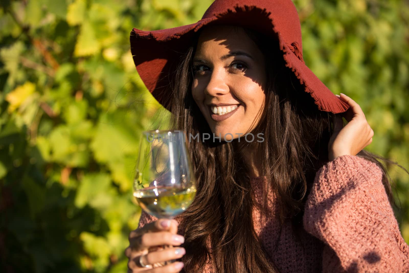 Smiling beautiful woman in a vineyard holding a glass of wine and looking at the camera.