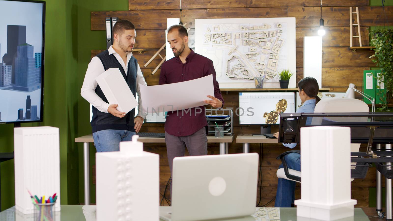 Slide view of focus transition with architects holding blue prints. Building models.