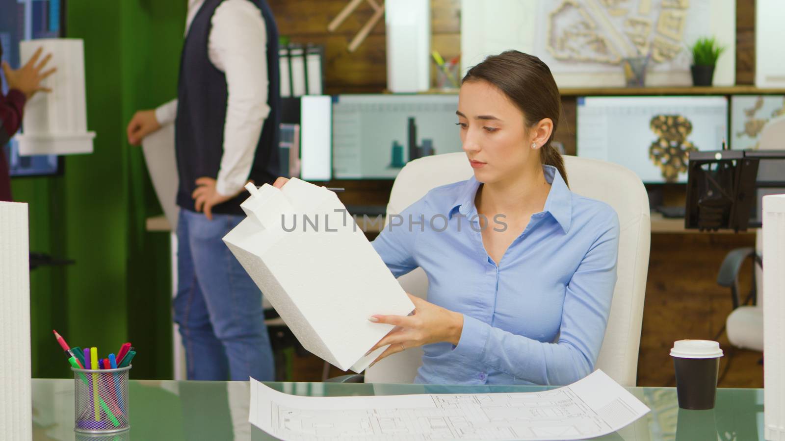 Young female architect working on a building project and taking a sip of coffee. Building model.