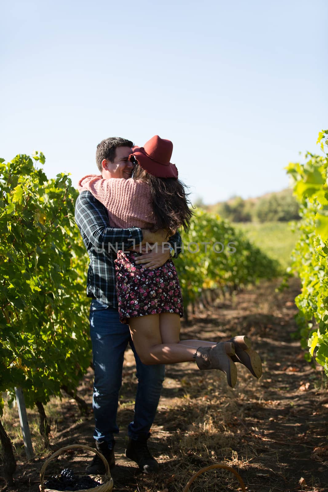 Romantic young man giving his beautiful girlfriend a big hug in a vineyard. Cheerful couple in vineyard.