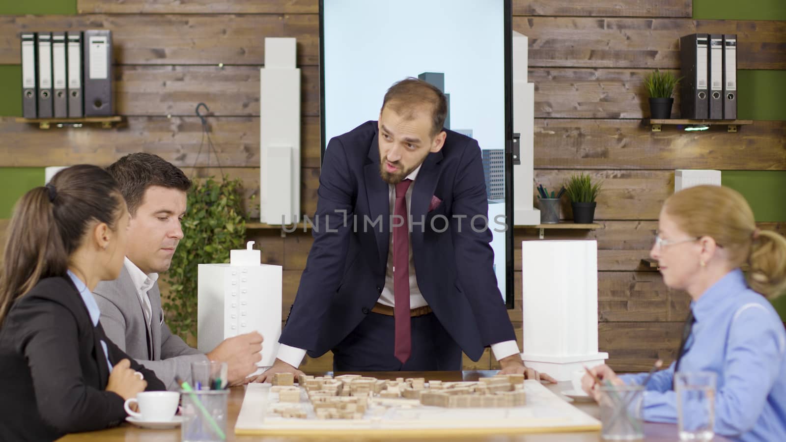 Architect in business suit leaning forward the table with mini town in the conference room. Team brainstorming.