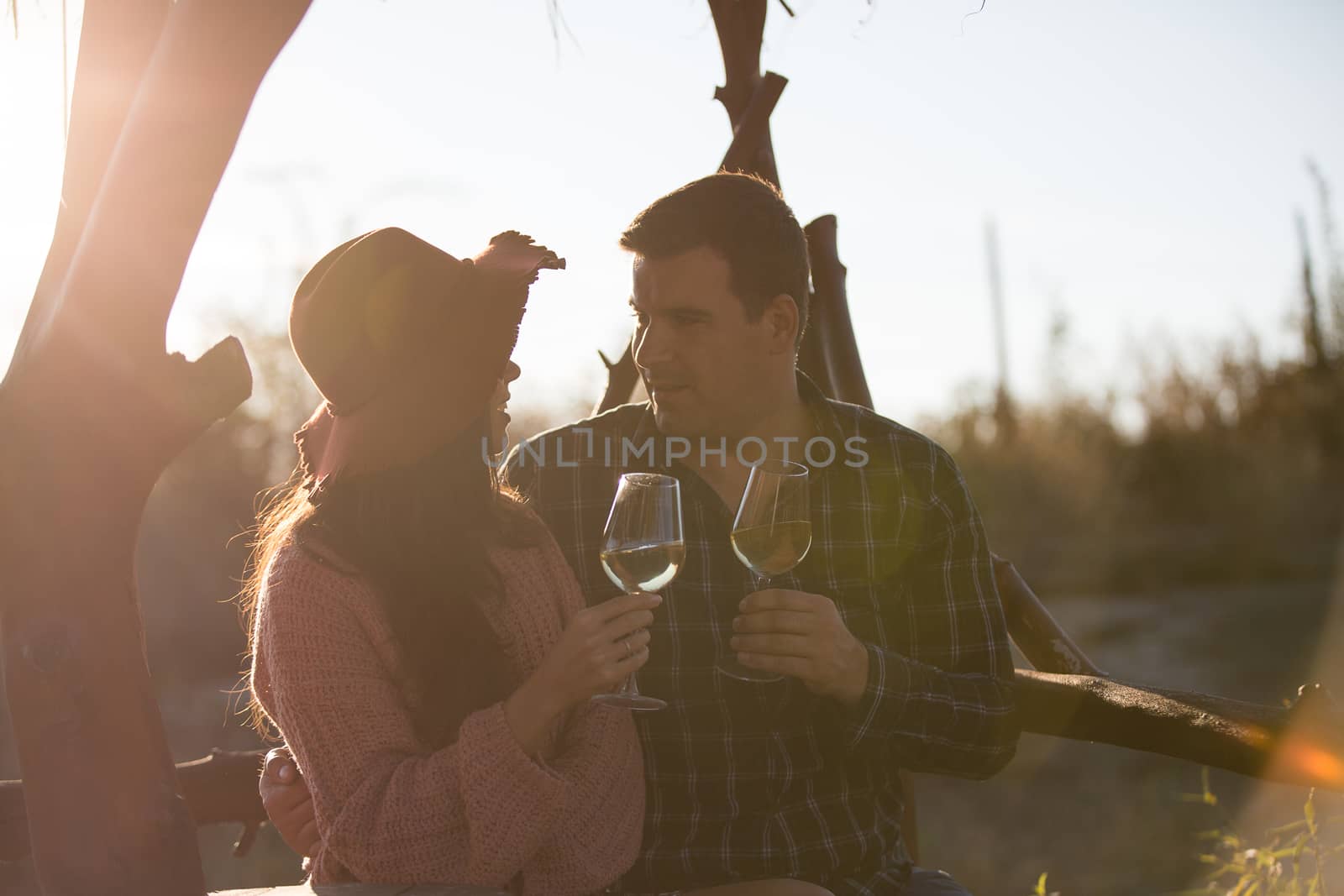Beautiful young couple talking and enjoying a glass of wine in a vineyard with sunset light from behind.