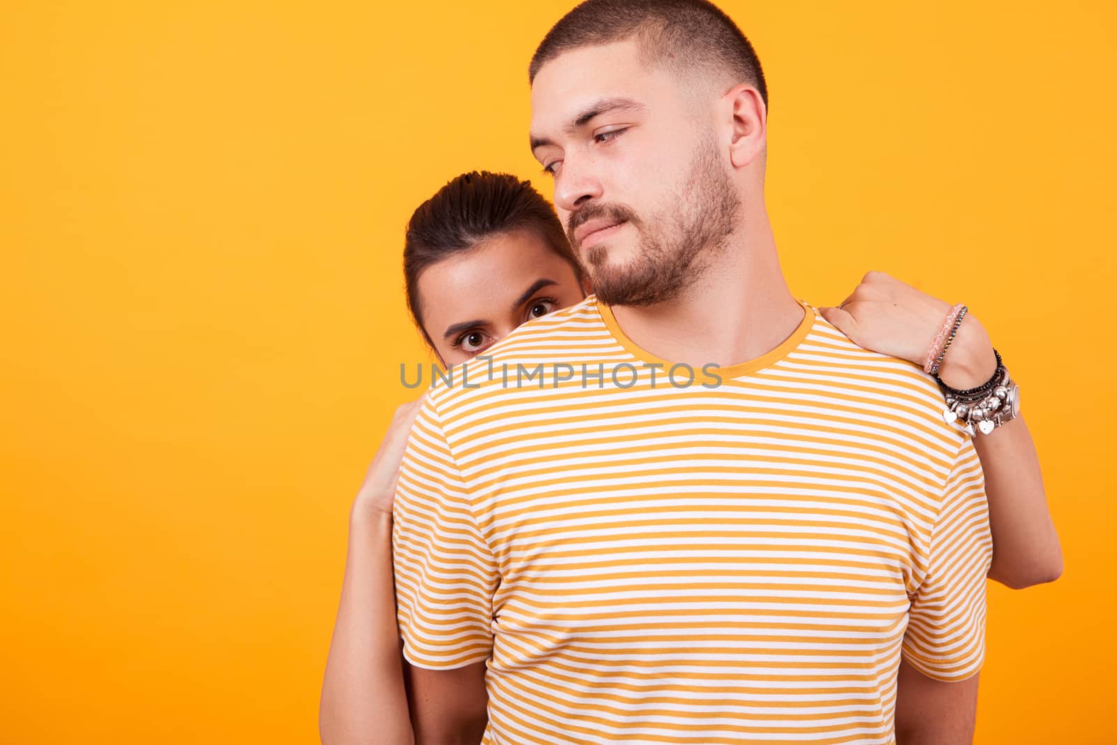Attractive girlfriend hiding behind her boyfriend back and looking at the camera.