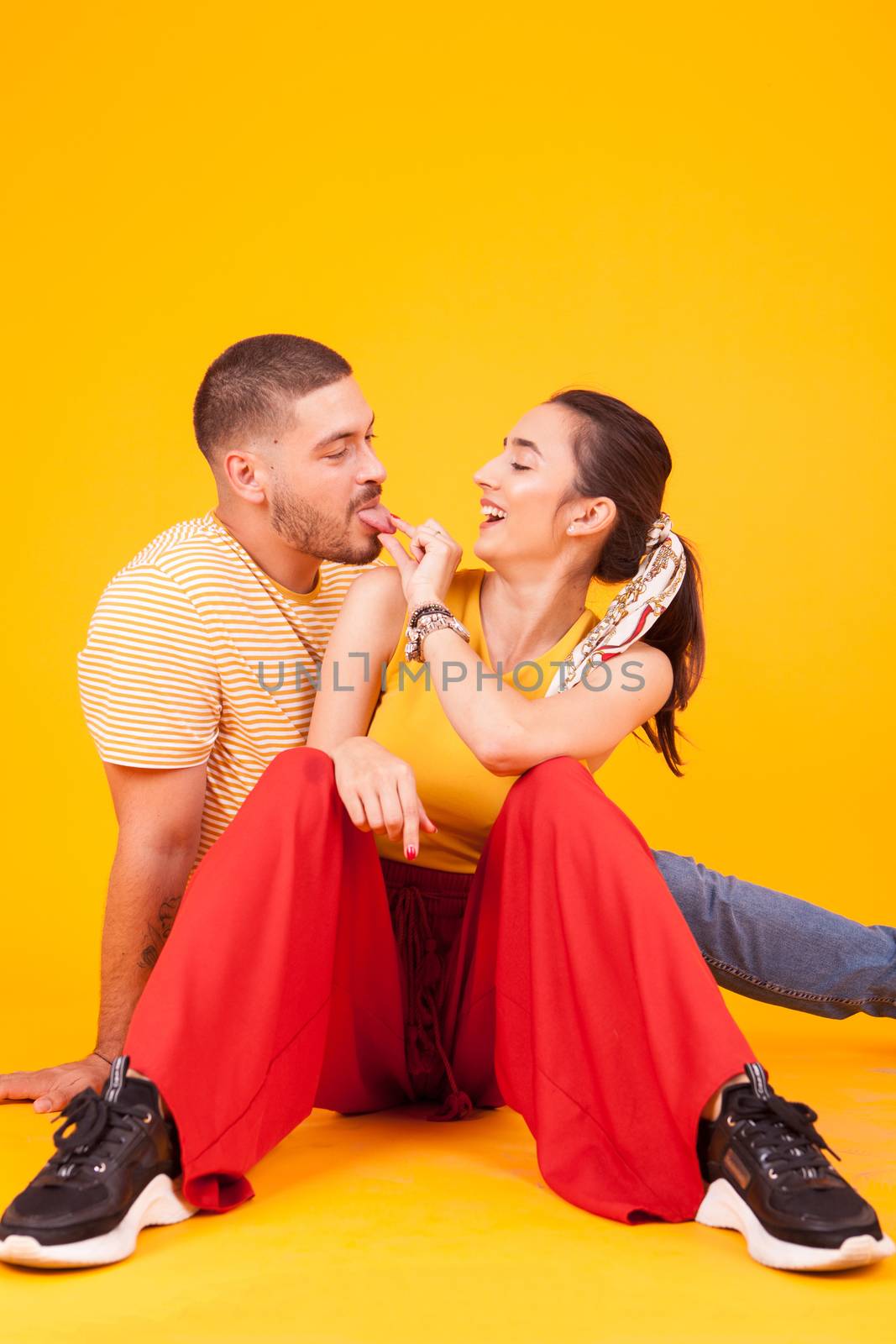Beautiful young couple acting silly in studio over yellow background. Attractive couple.