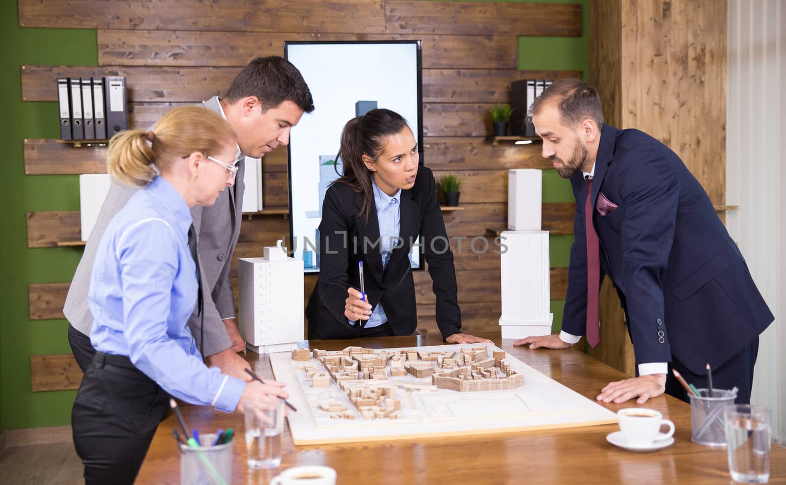 Female construction engineers working together with team of architects in conference room. Mini town. Architect in business suit.
