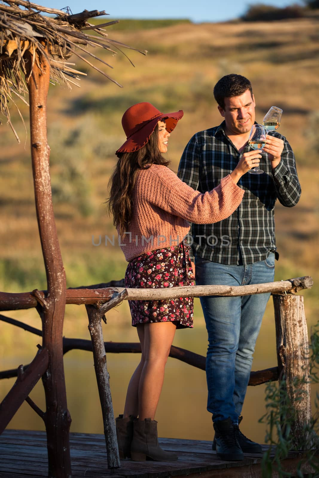 Couple of wine tasters looking at the color of the wine on a wooden pontong by the edge of a lake