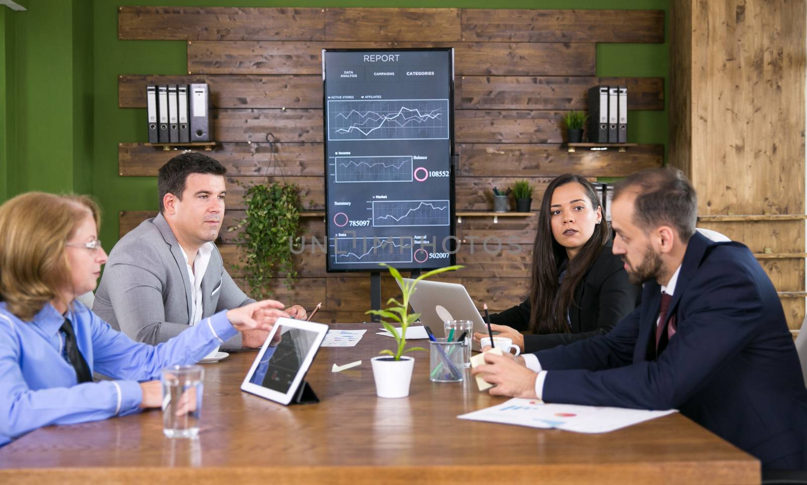 Team of business people having a meeting in the conference room with charts on tv screen.