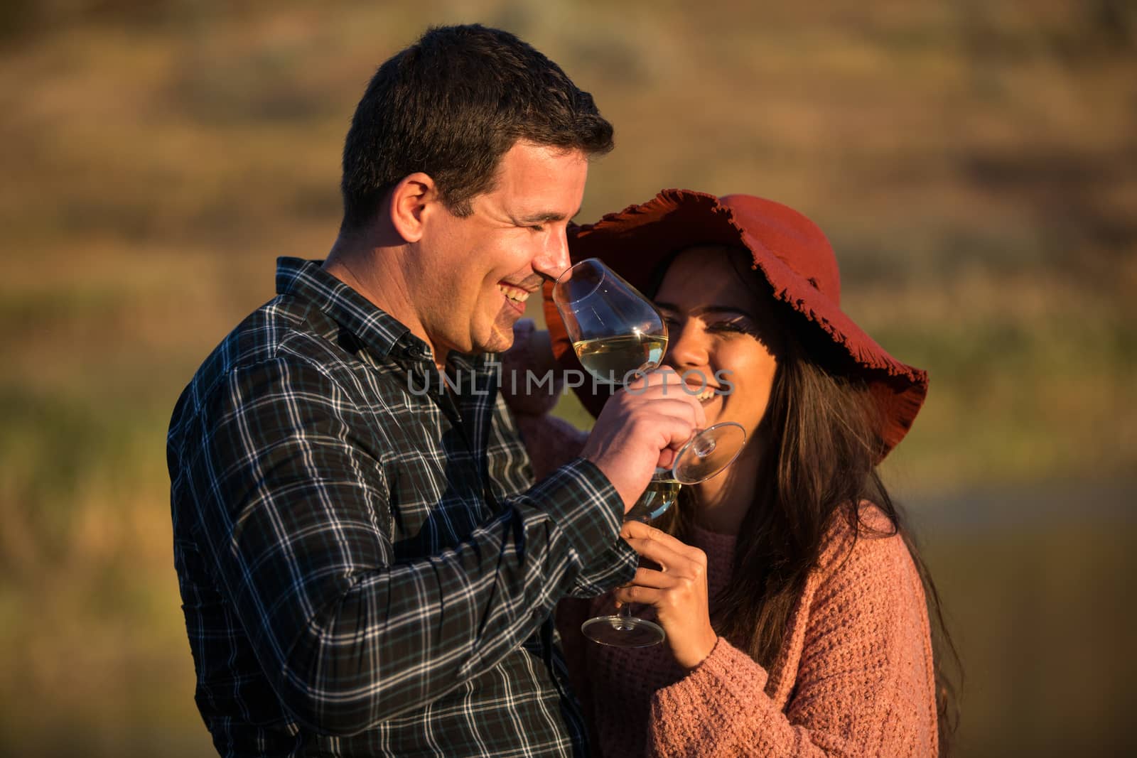 Man and woman with glasses of wine in his hands on the sunset in a vineyard.