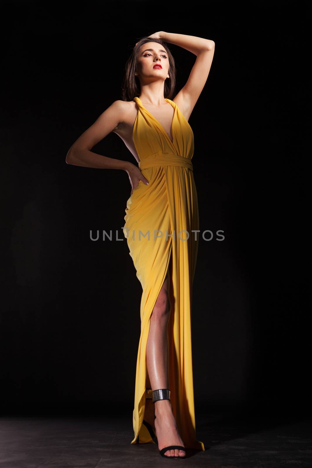 Pretty beautiful young fashion model wearing stylish yellow long dress. Fashion model posing in studio over black background.