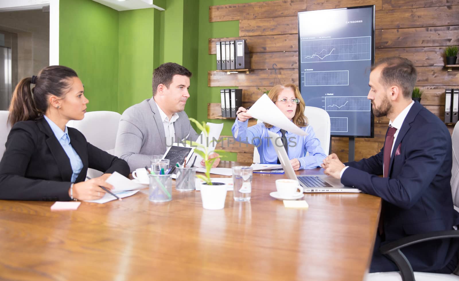 Discussion between business people in a conference room with charts on tv screen.