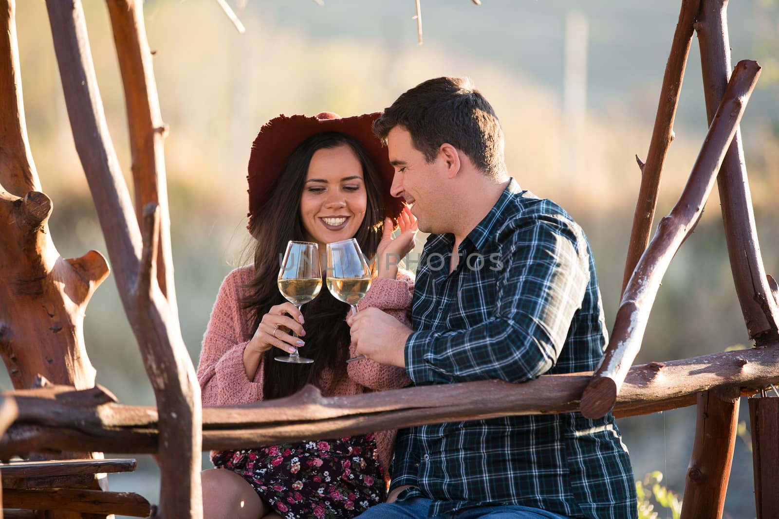 Couple sitting on a wooden pontont at the edge of a lake in the middle of a vineyard dinking a glass of wine.