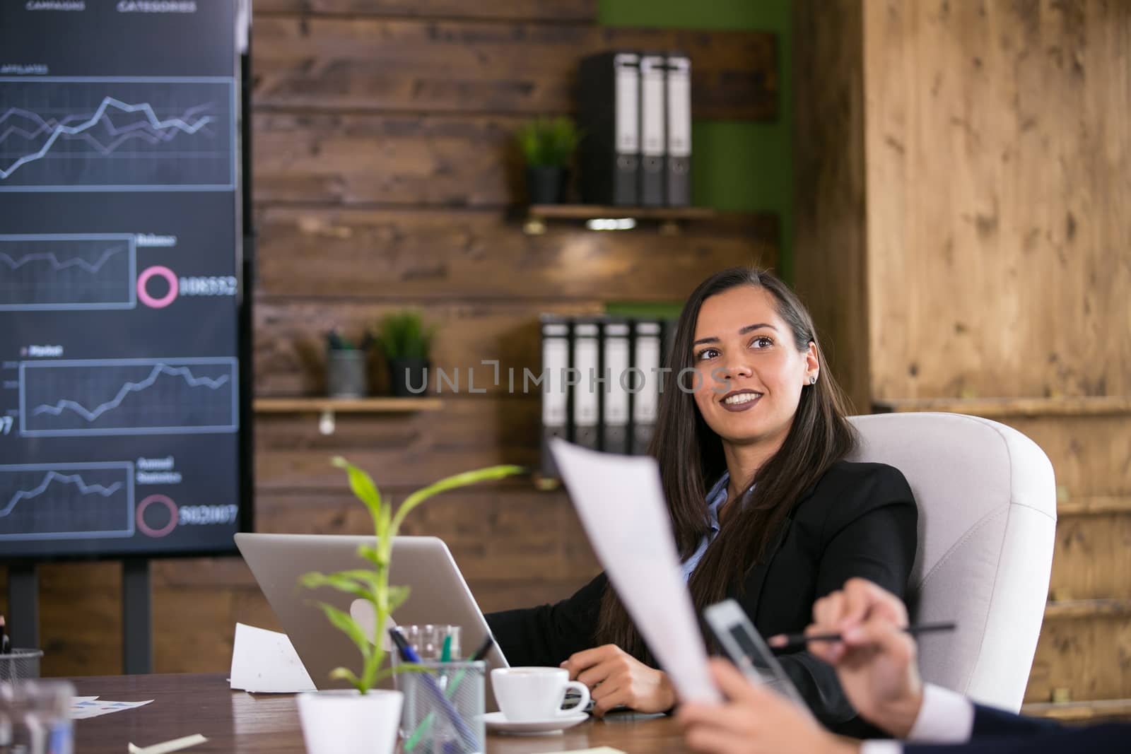 Business young woman wearing a suit in conference room and charts on tv screen.