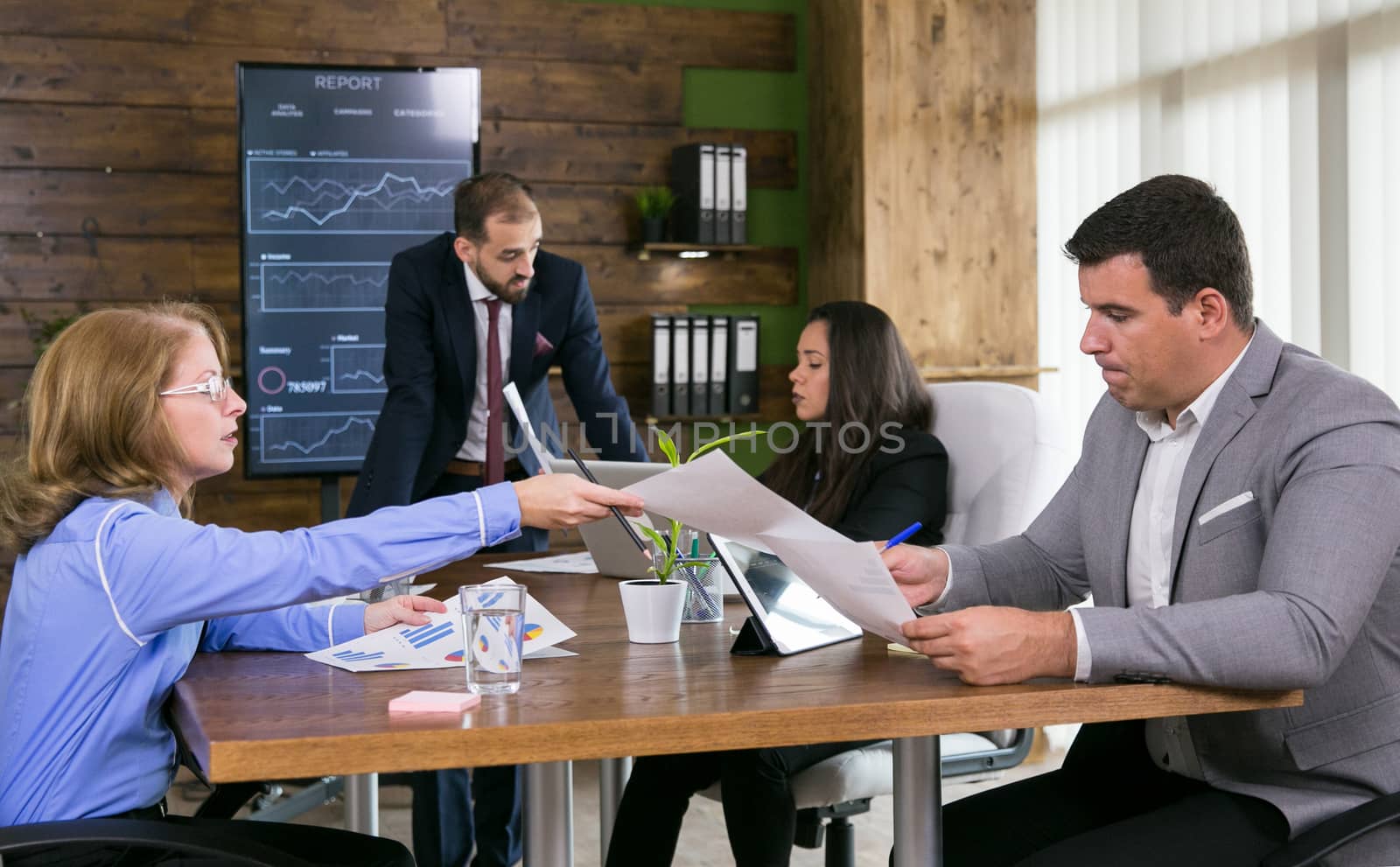 Middle age business woman giving charts to her young colleague in the conference room.