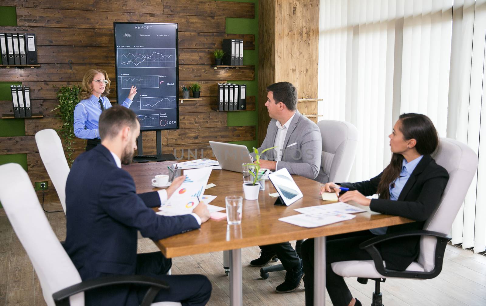 Middle age business woman presenting charts to colleagues in conference room.