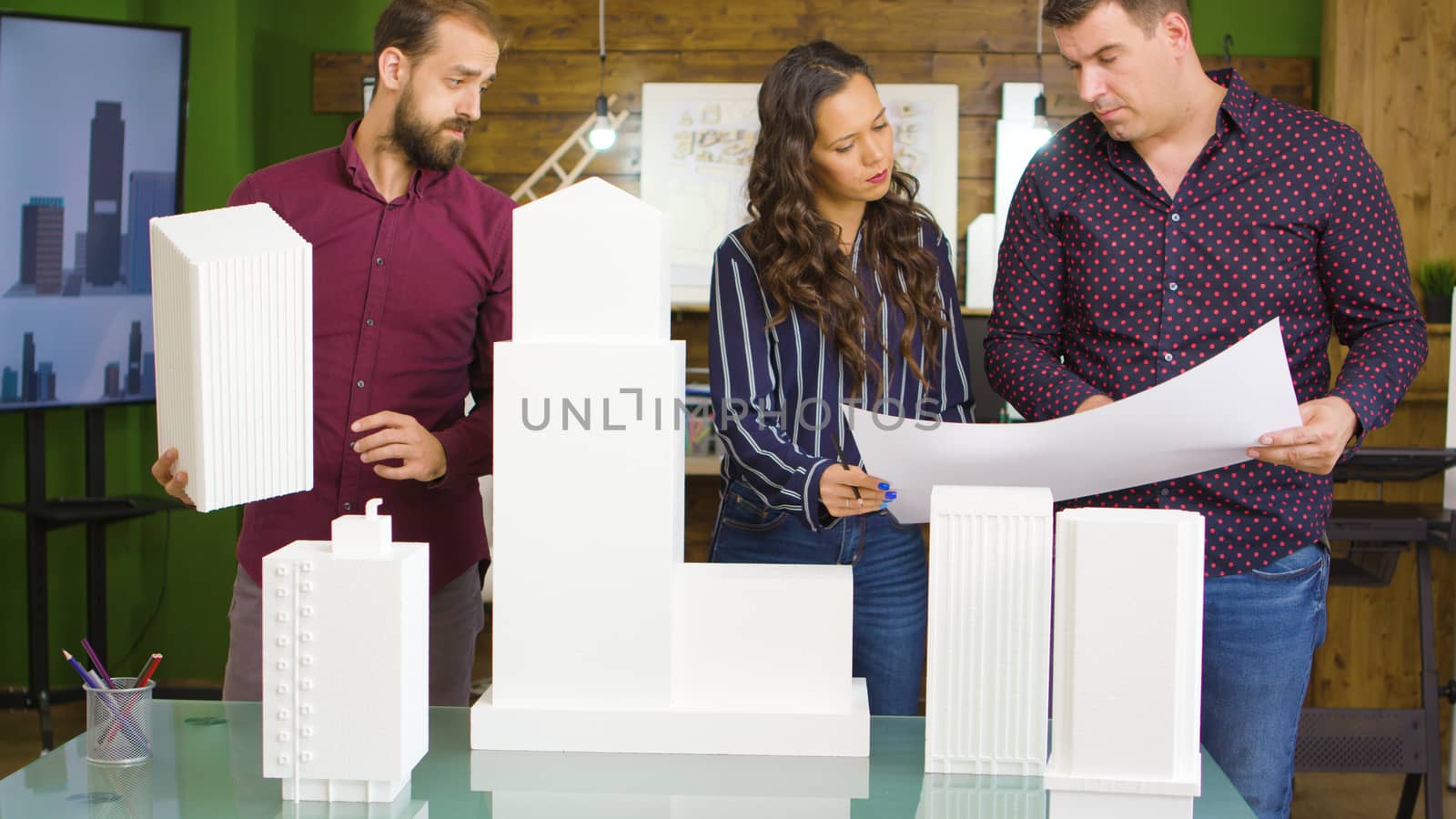 Team of architects working with blueprints and 3D printed models of buildings in modern cozy office