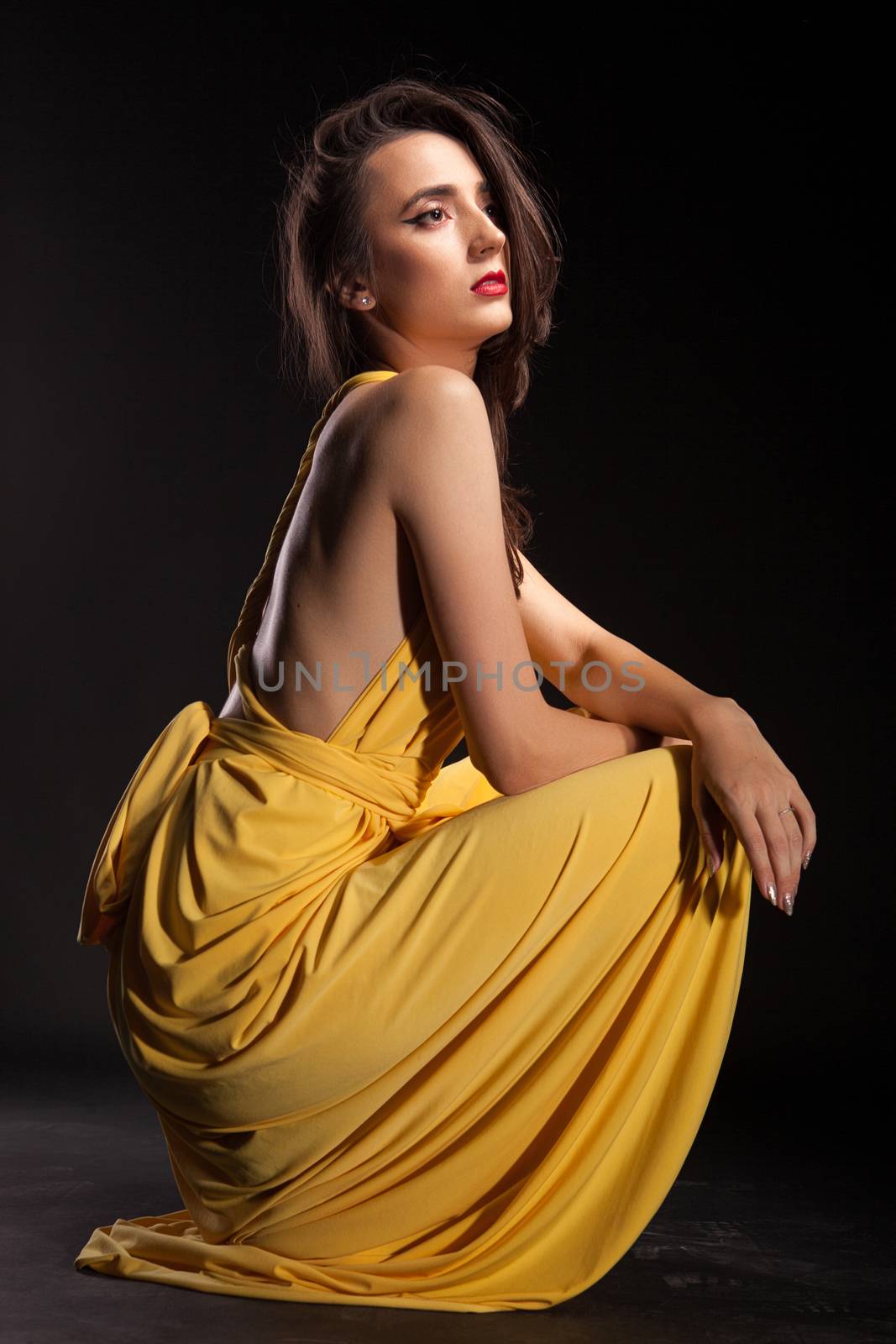 Young fashion model posing in stylish yellow dress looking into the light over black background.