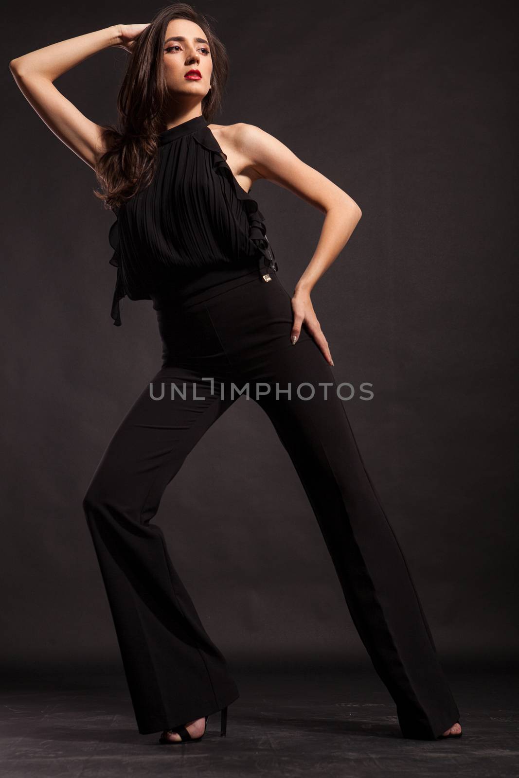 Beautiful fashion model wearing black pants posing in studio over black background. Gorgeou fashion model.