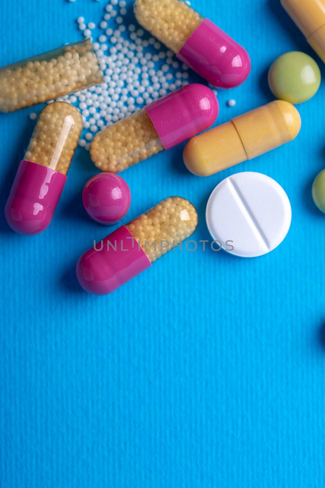 Top view with a white pill surrounded by purple and yellow capsules. Copy space and blue background