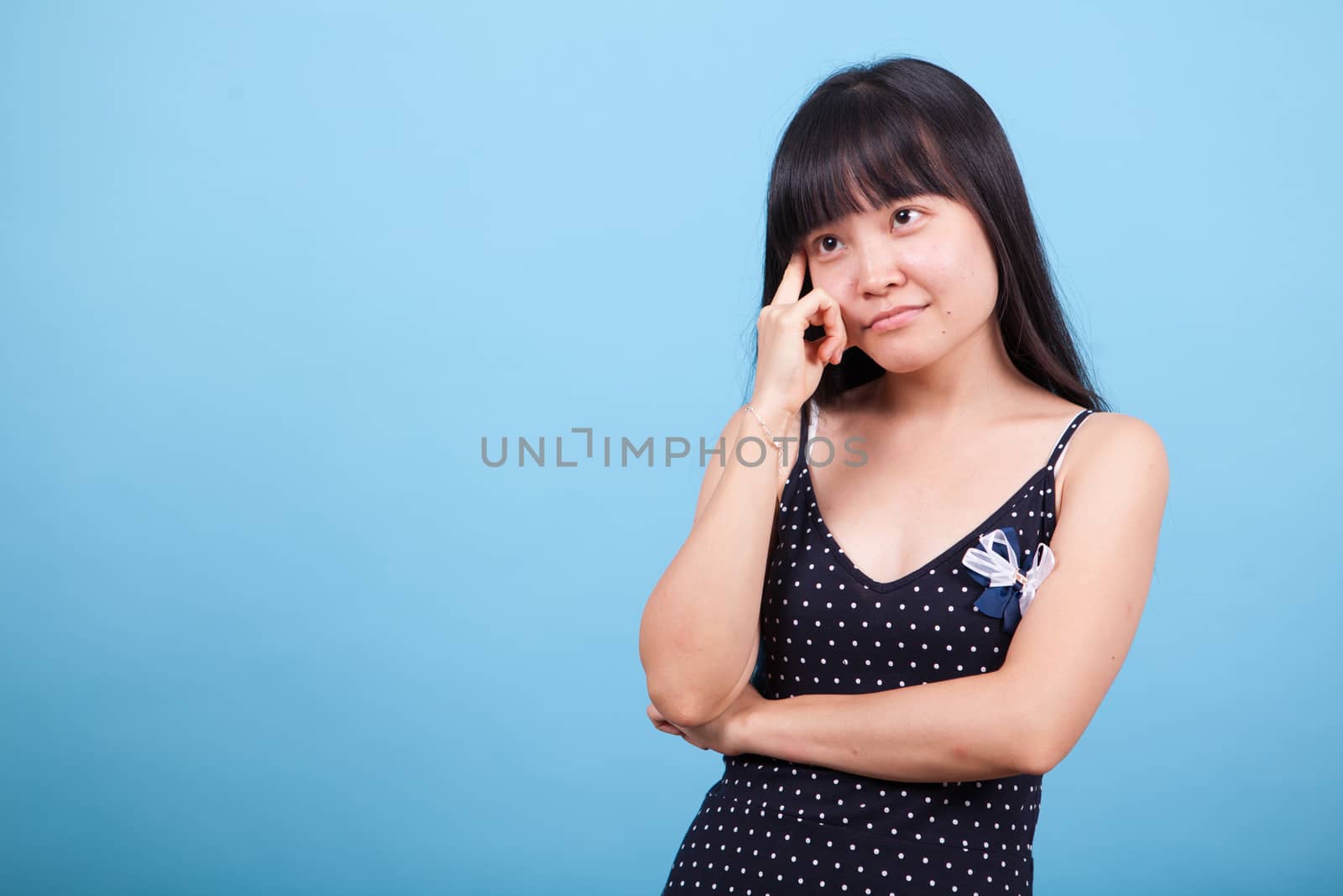 Portrait of thoughtful asian girl in studio over blue background. Asian girl thinking.