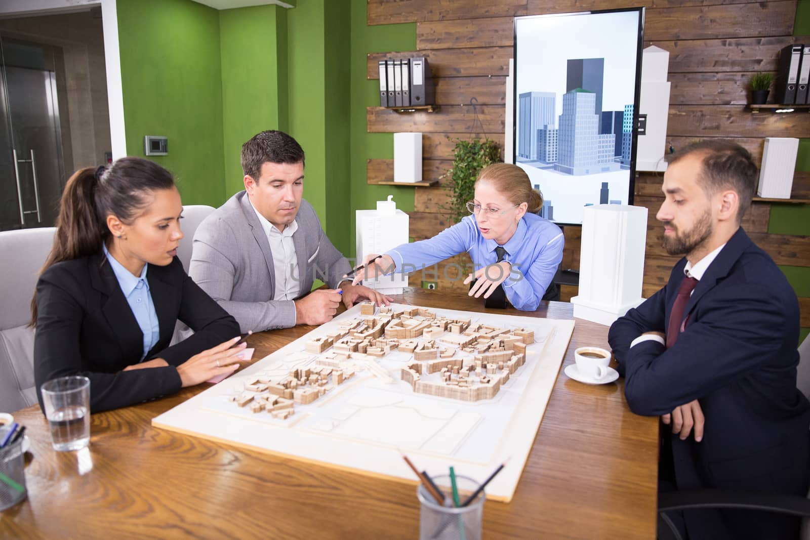 Middle age female architect pointing at town project.Team of architects.