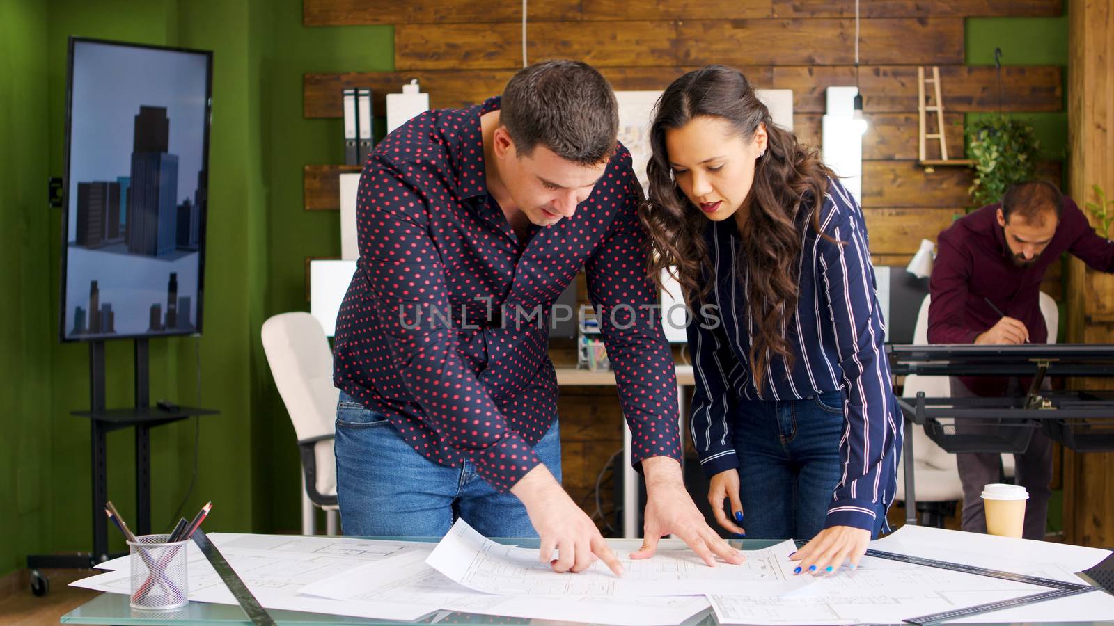 Female architects and male constructor looking at blueprints in cozy modern office