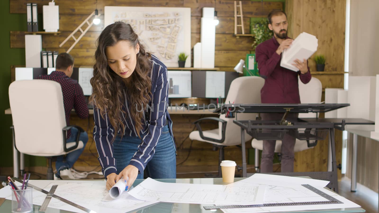 Woman designer in creative media agency lookign at blueprints in modern office