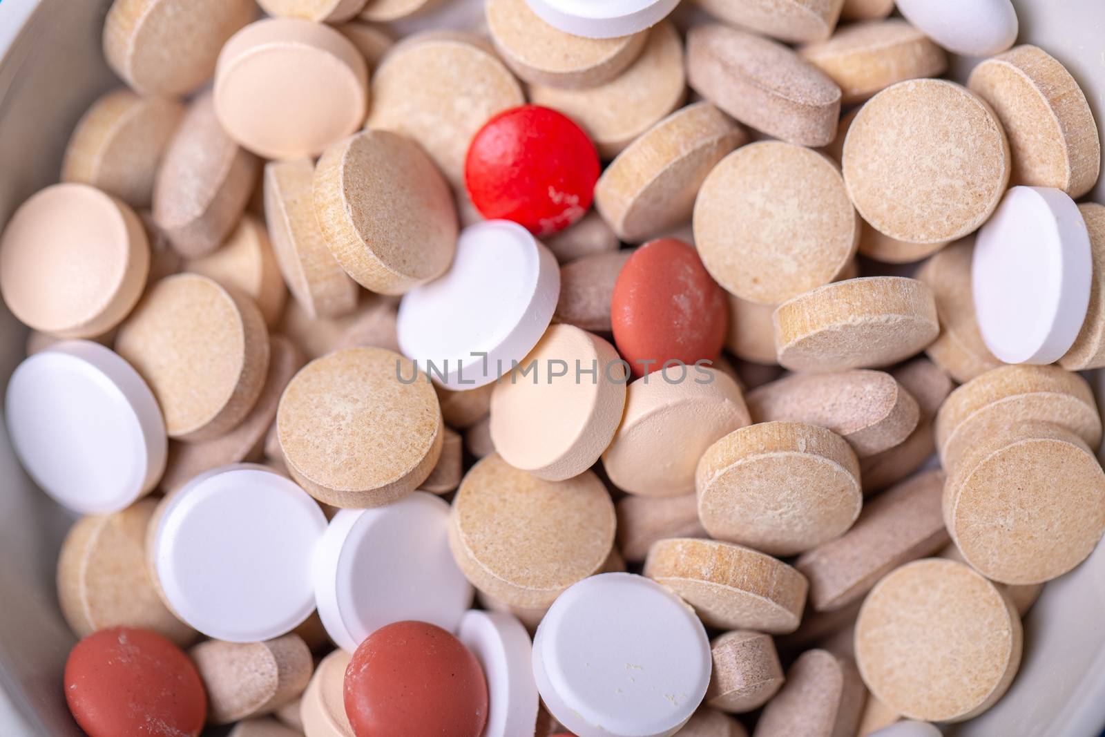 Close up with a red pill among several pills of different colors. Macro and red color
