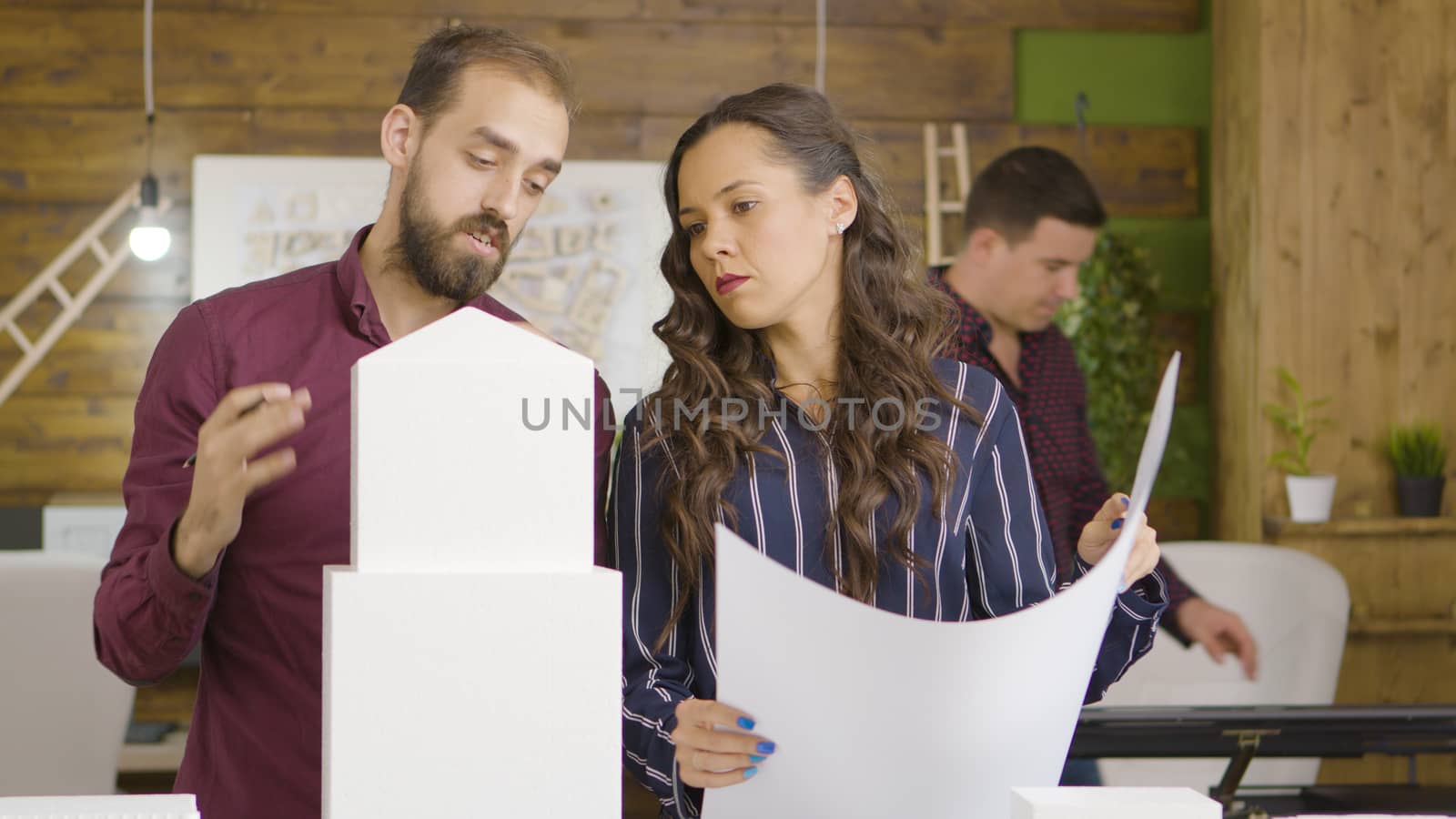 Female and male architects talking near 3D models of buildings in creative media agency