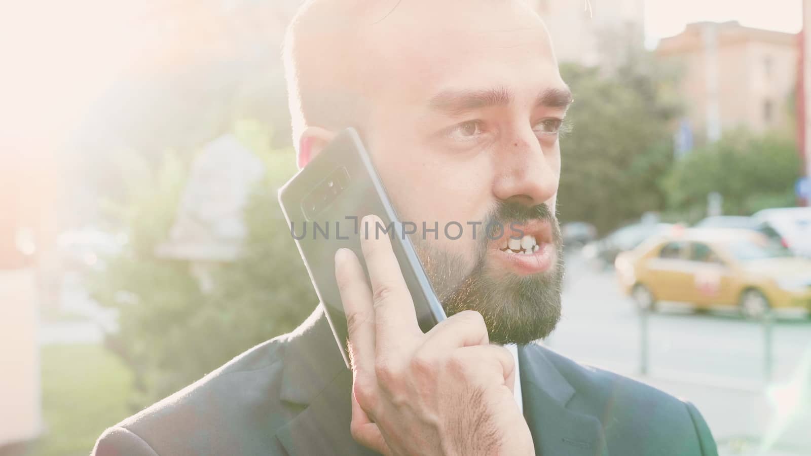 Portrait of handsome businessman talking on the phone while lens flares are hitting the screen. Slow motion close up