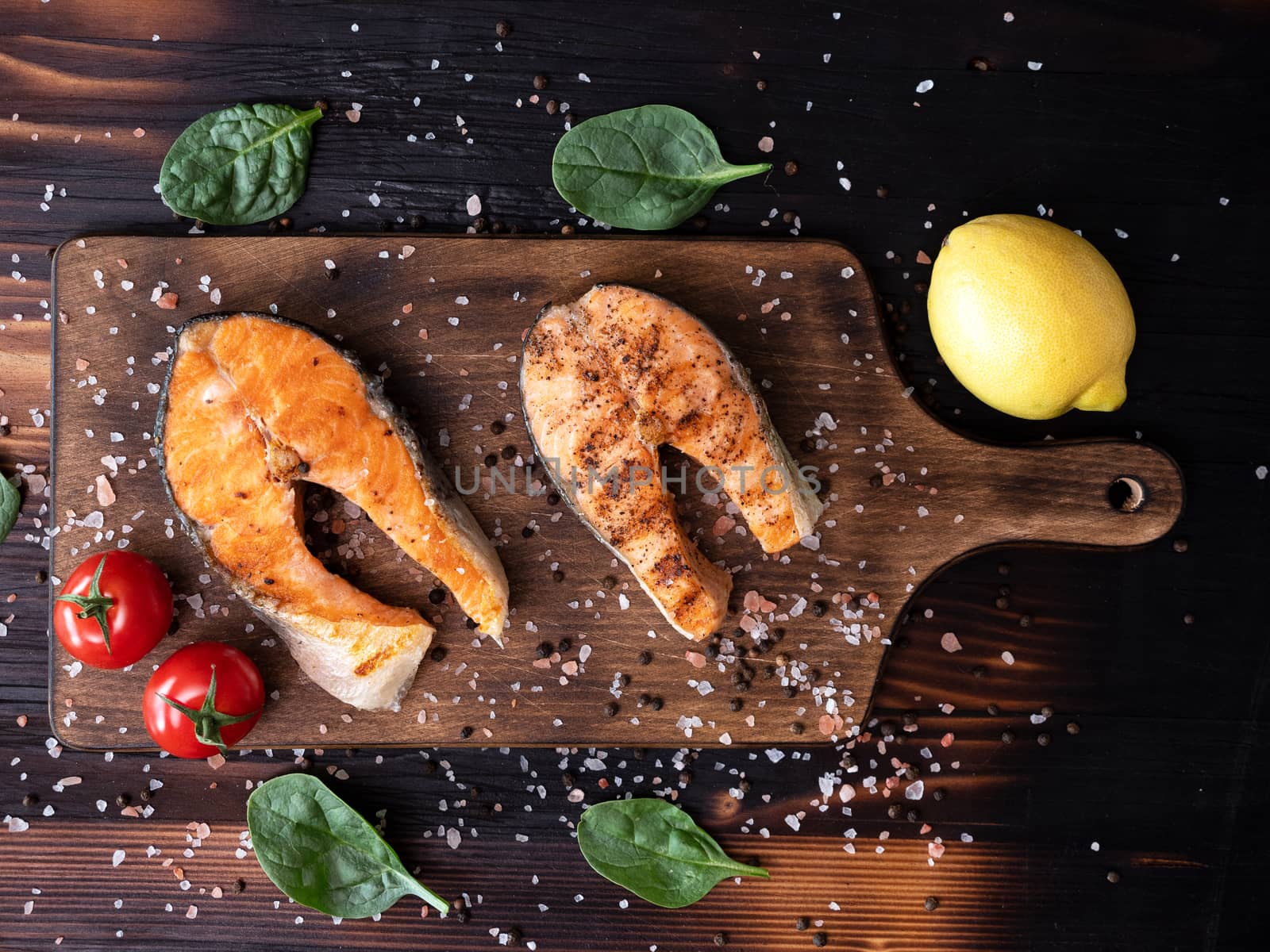 Top view of wooden bottom on which two salmon rings are arranged.Tomatoes and lemon