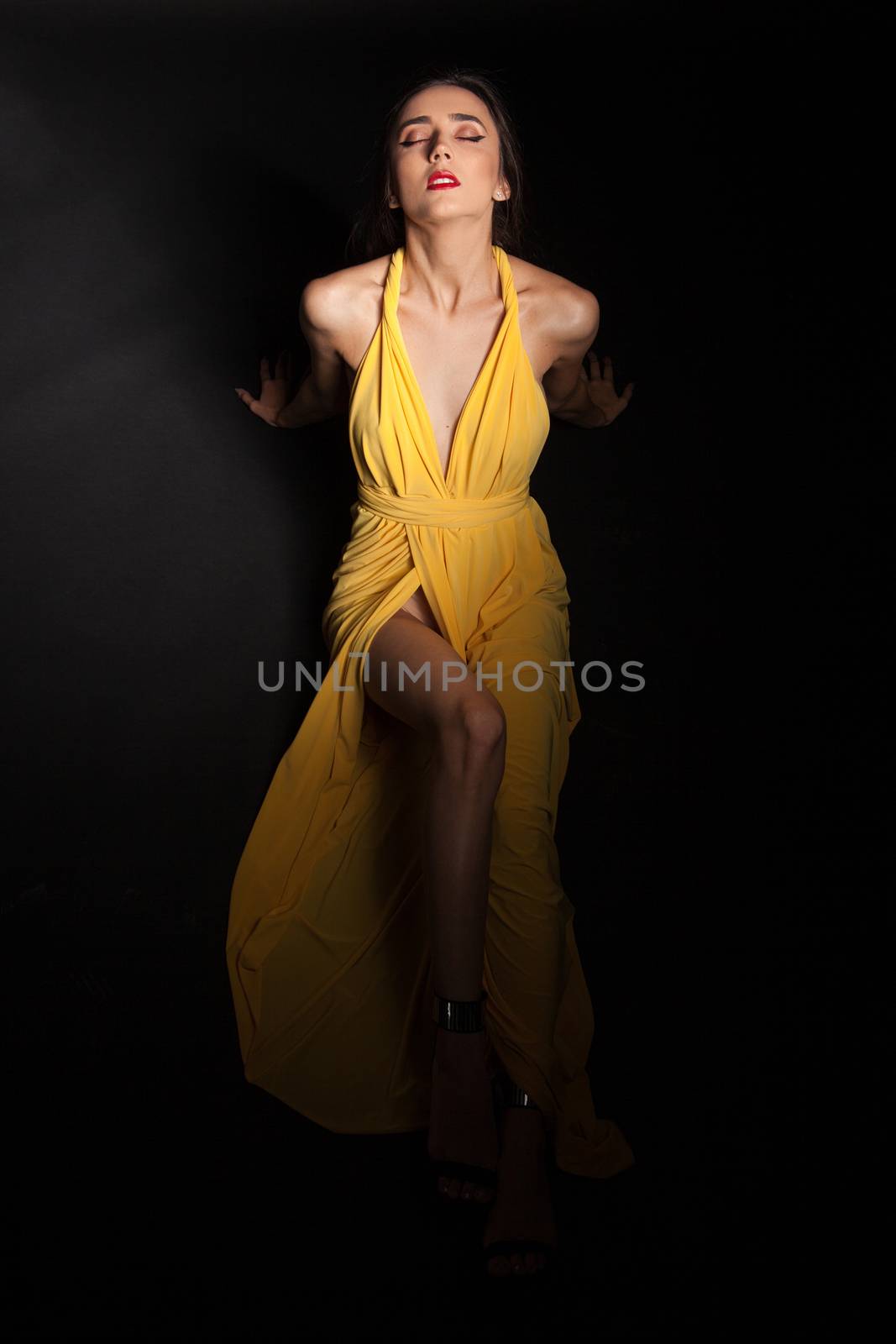 Glamorous fashion model posing in studio wearing stylish yellow dress. Attractive fashion model.