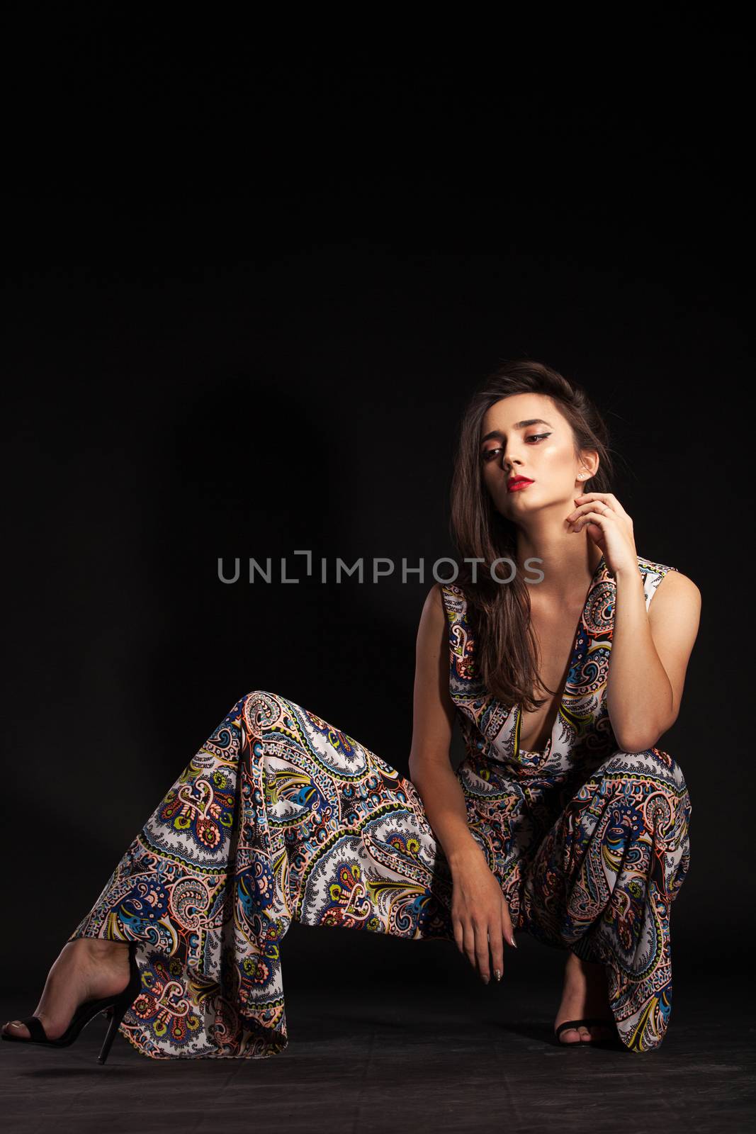 Stylish fashion model posing in studio wearing colorful pants over black background. Brunette fashion model.