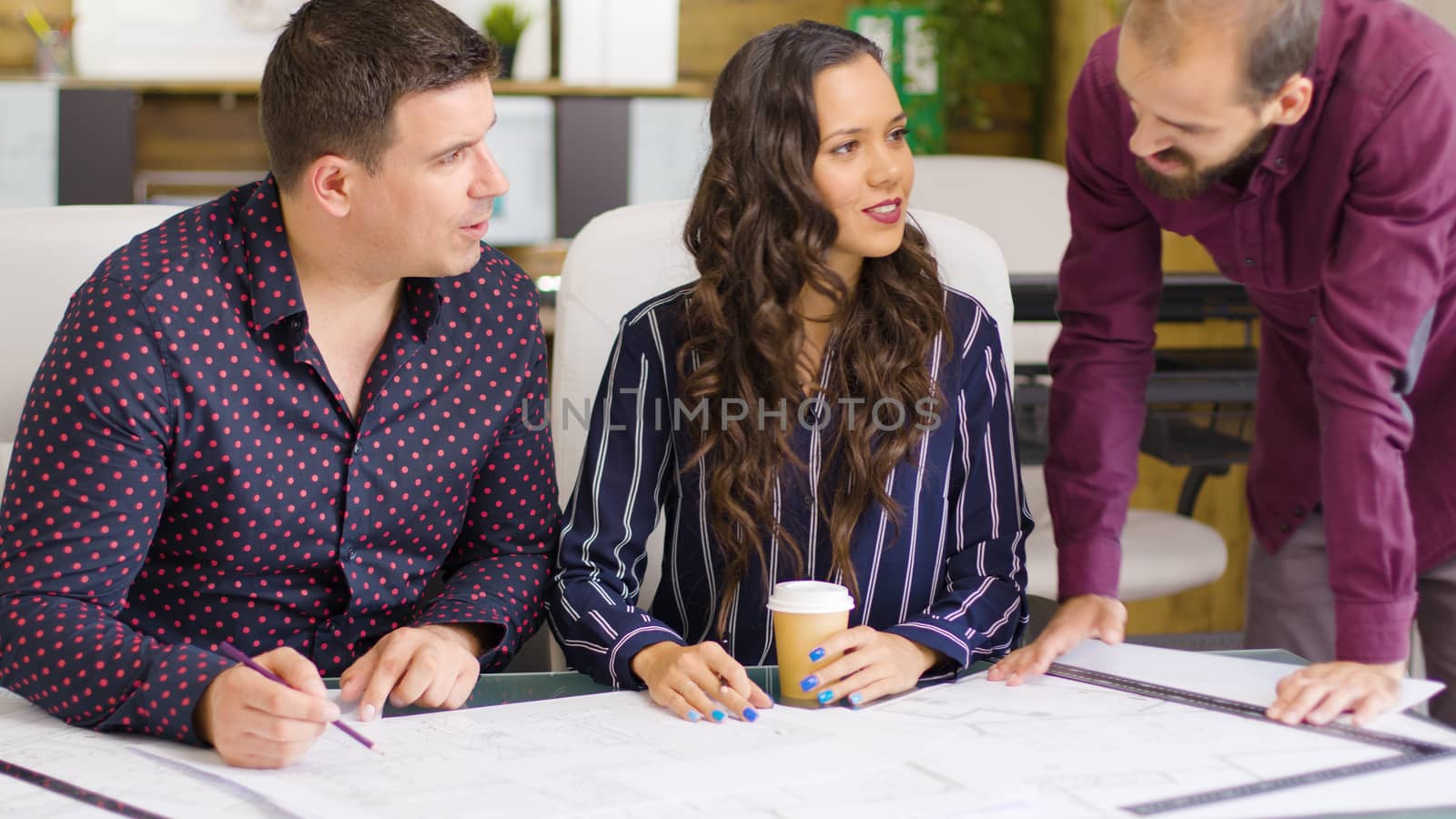 Three architects and designers talking about blue prints that are on the table