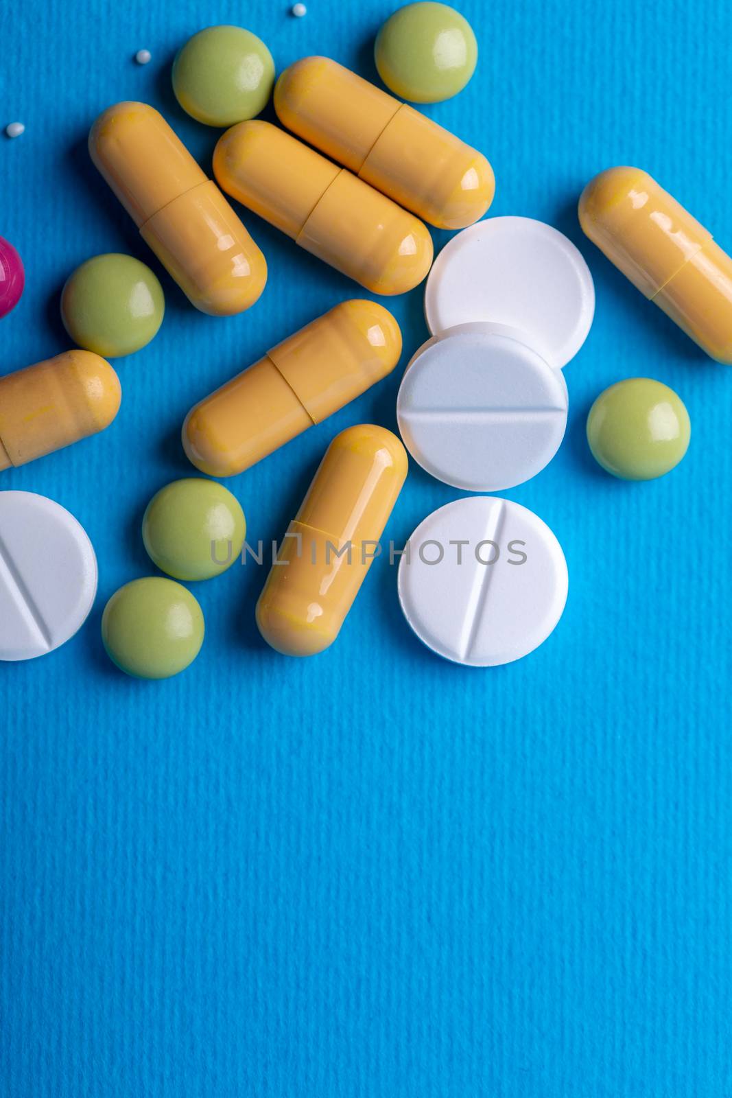Top view with white pills surrounded by yellow capsules and green pills. Copy space and blue background