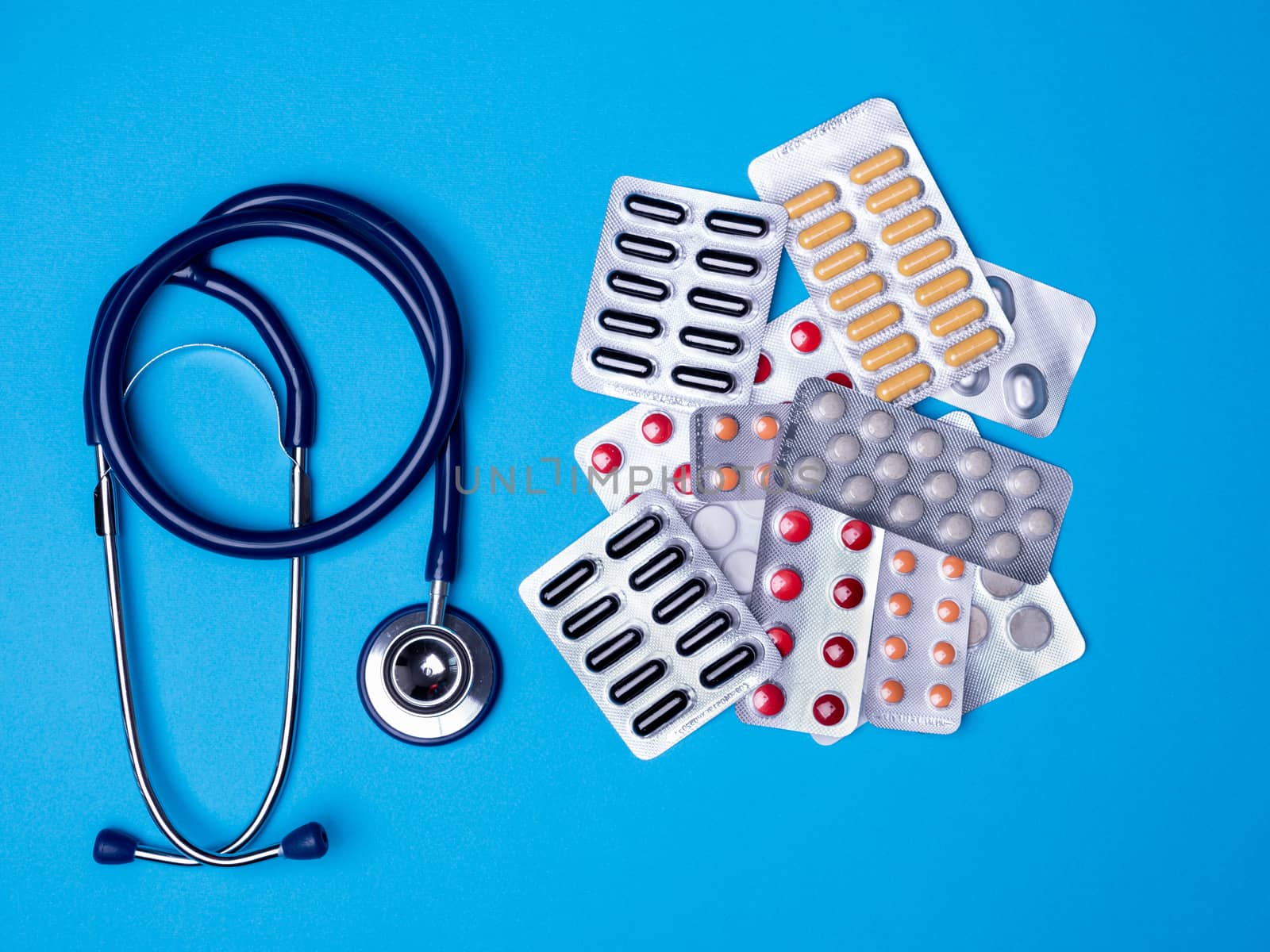Top view with a stethoscope and blisters with multicolored pills. Copy space and blue background