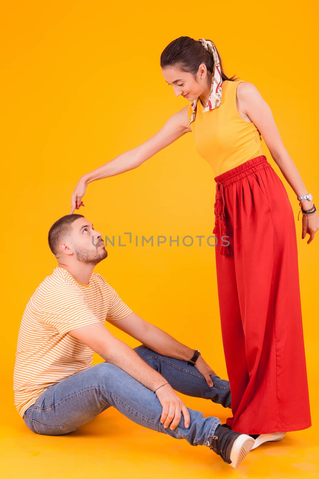 Happy and funny young couple in studio over yellow background.