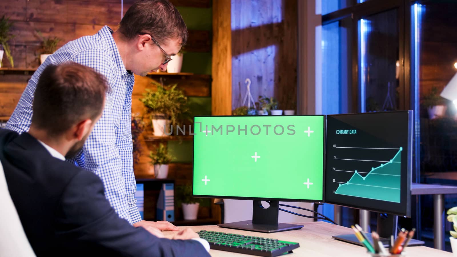 Two office colleagues looking at a green computer screen. Moon light and blue light