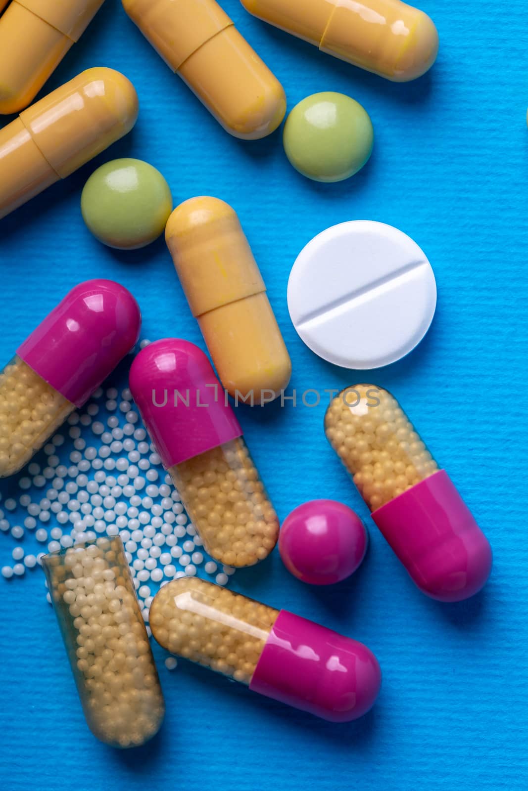 Top view with a white pill surrounded by capsules and multicolored pills. Blue background