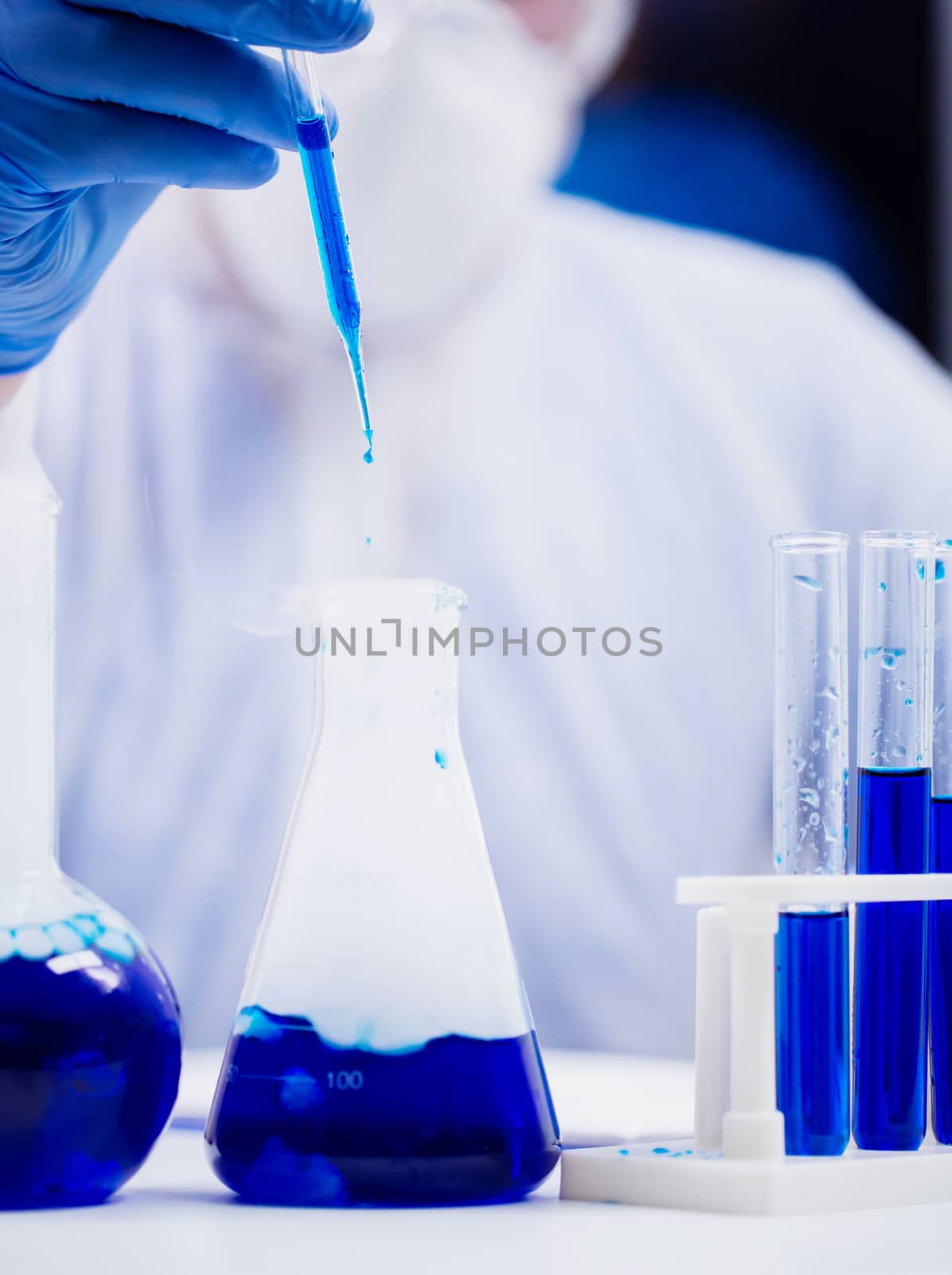 Scientist in a research laboratory taking a sample of blue solution using a pipette.